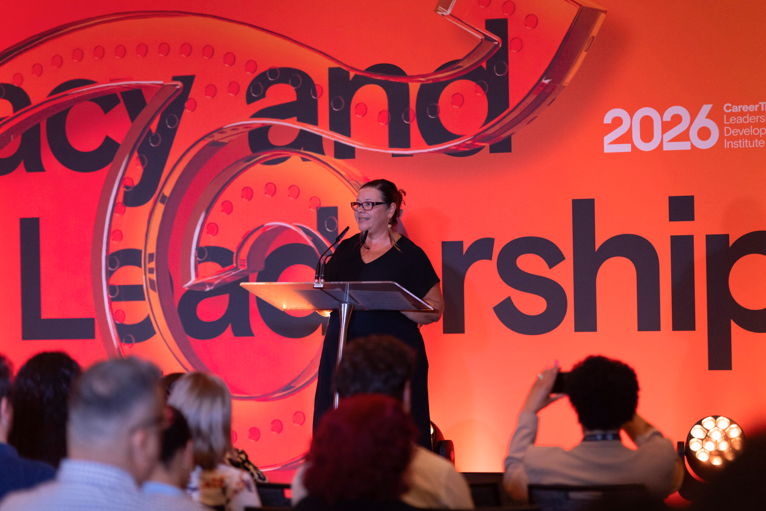 A CareerTrackers speaker addressing the audience from the stage at the Leadership Development Institute, framed by a bold "Legacy and Leadership" backdrop.