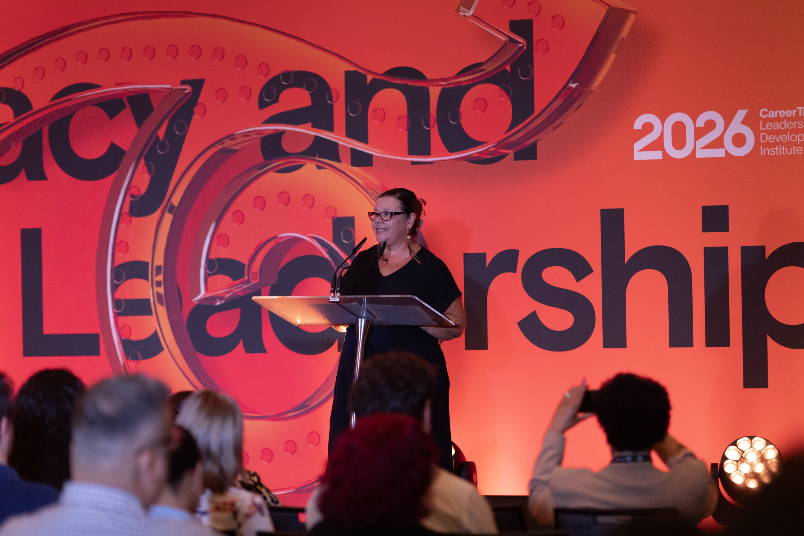 A CareerTrackers speaker addressing the audience from the stage at the Leadership Development Institute, framed by a bold "Legacy and Leadership" backdrop.